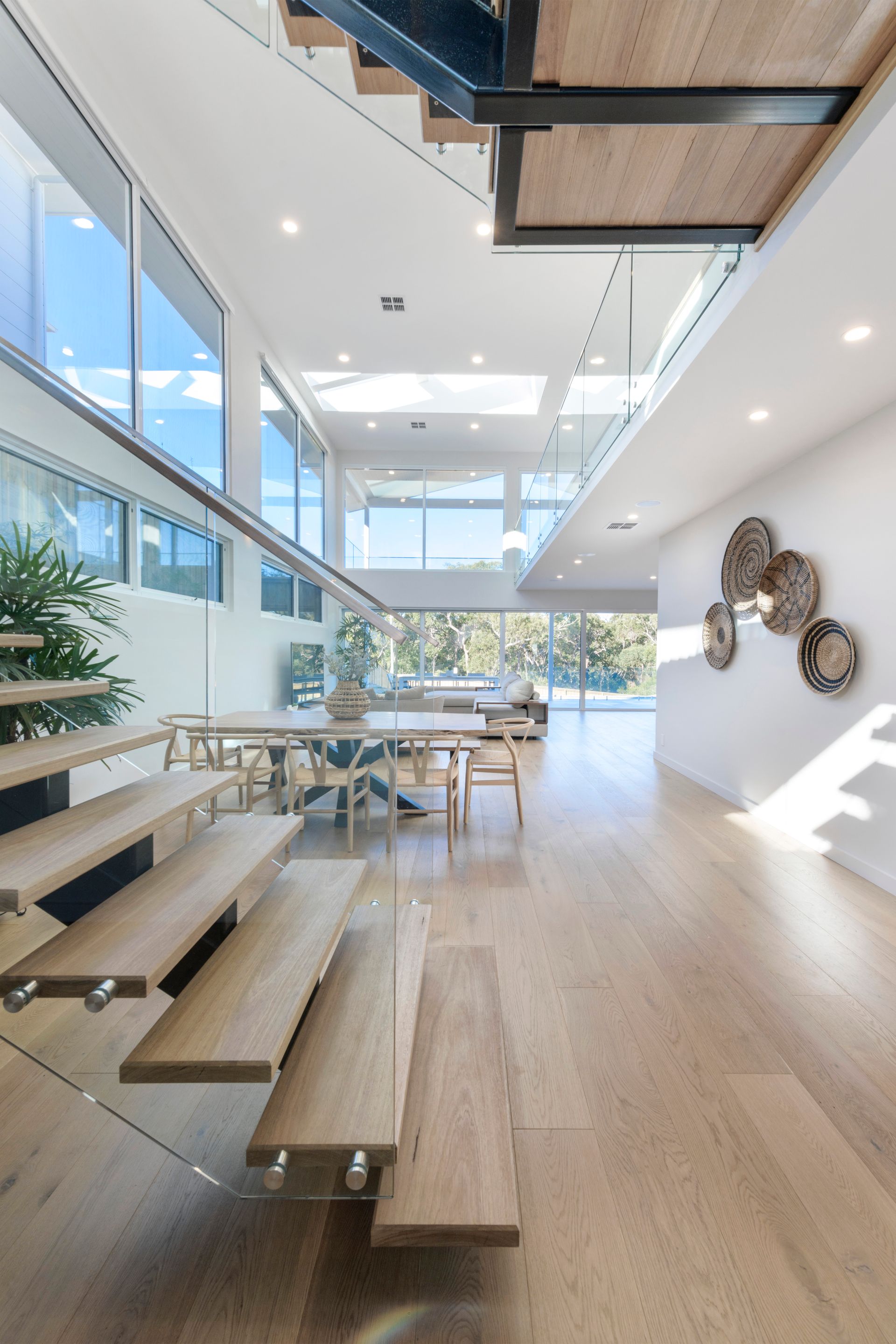 Floating wooden staircase in a modern home with light wood floors, glass walls, and natural light — Indie Living In Bennetts Green, NSW