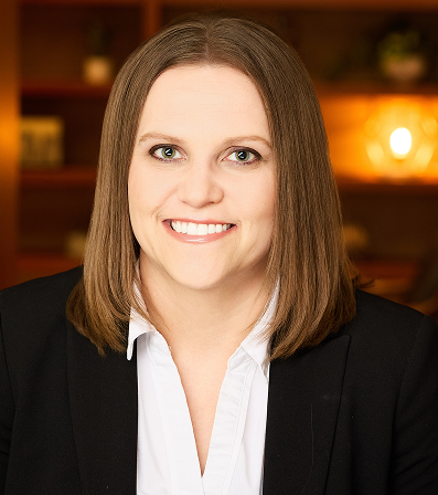 Woman in a black blazer and white shirt, smiling, in a warm-lit indoor setting.