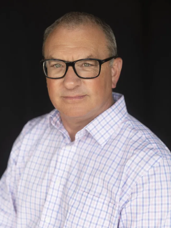Man in glasses and blue suit smiles in an office setting.