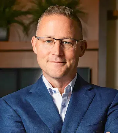 Man in glasses and blue suit smiles in an office setting.