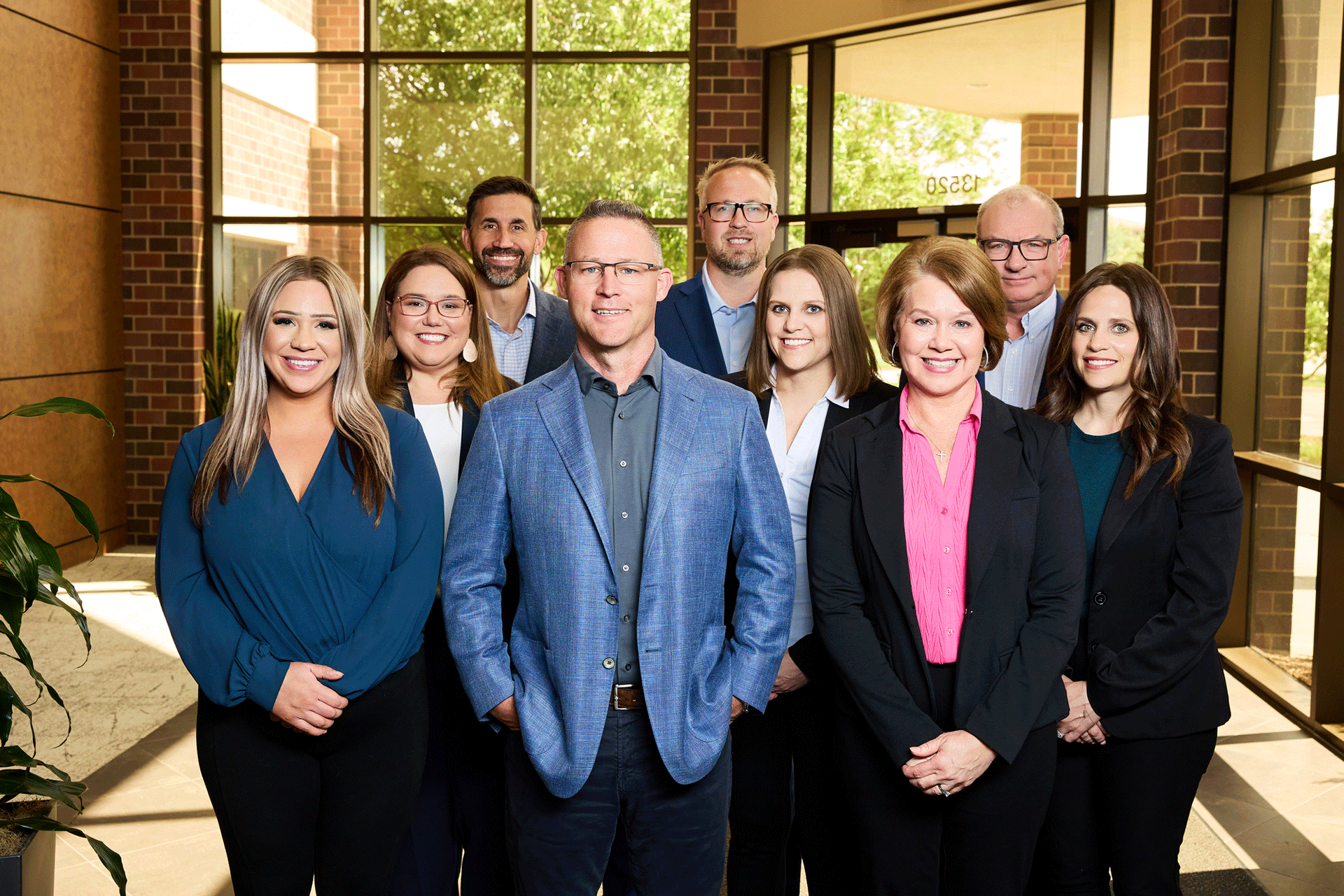 Group of 10 people posing for a photo in front of a building. They are wearing business attire.