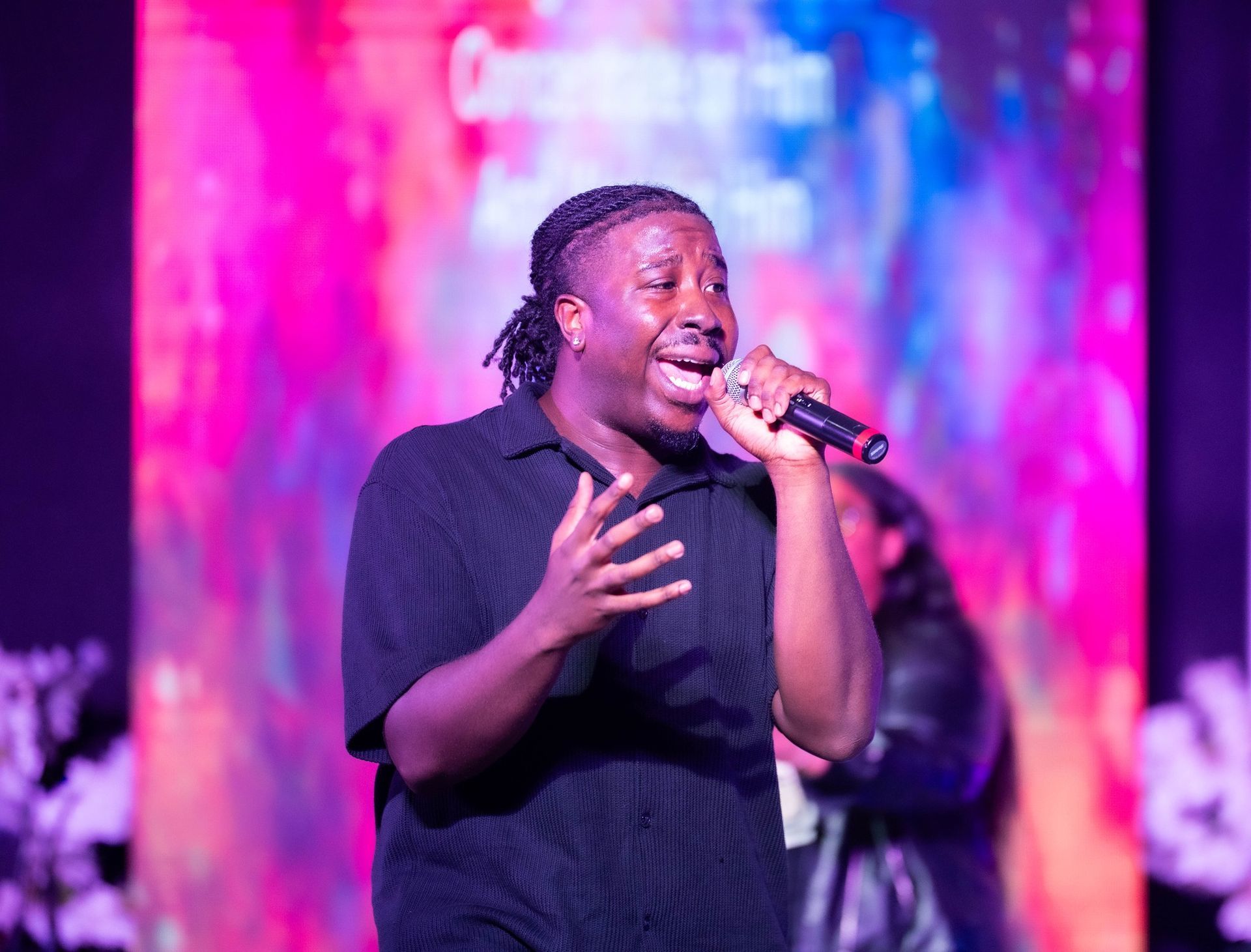 Man singing into a microphone onstage; colorful, abstract background.