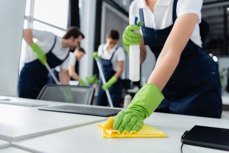 In un luminoso spazio di lavoro, gli addetti alle pulizie puliscono un tavolo con panni gialli e verdi.