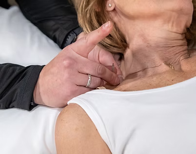 Hands gently touching the neck of a seated person in a white shirt during a medical exam.