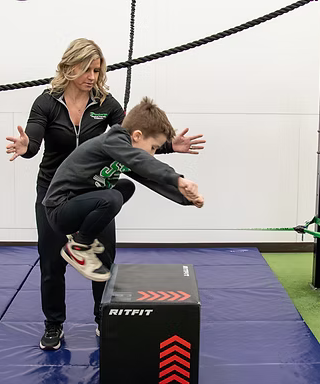 Woman coaches child jumping off a box in an indoor gym training area