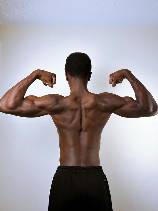 Person flexing back and arm muscles against a plain white background