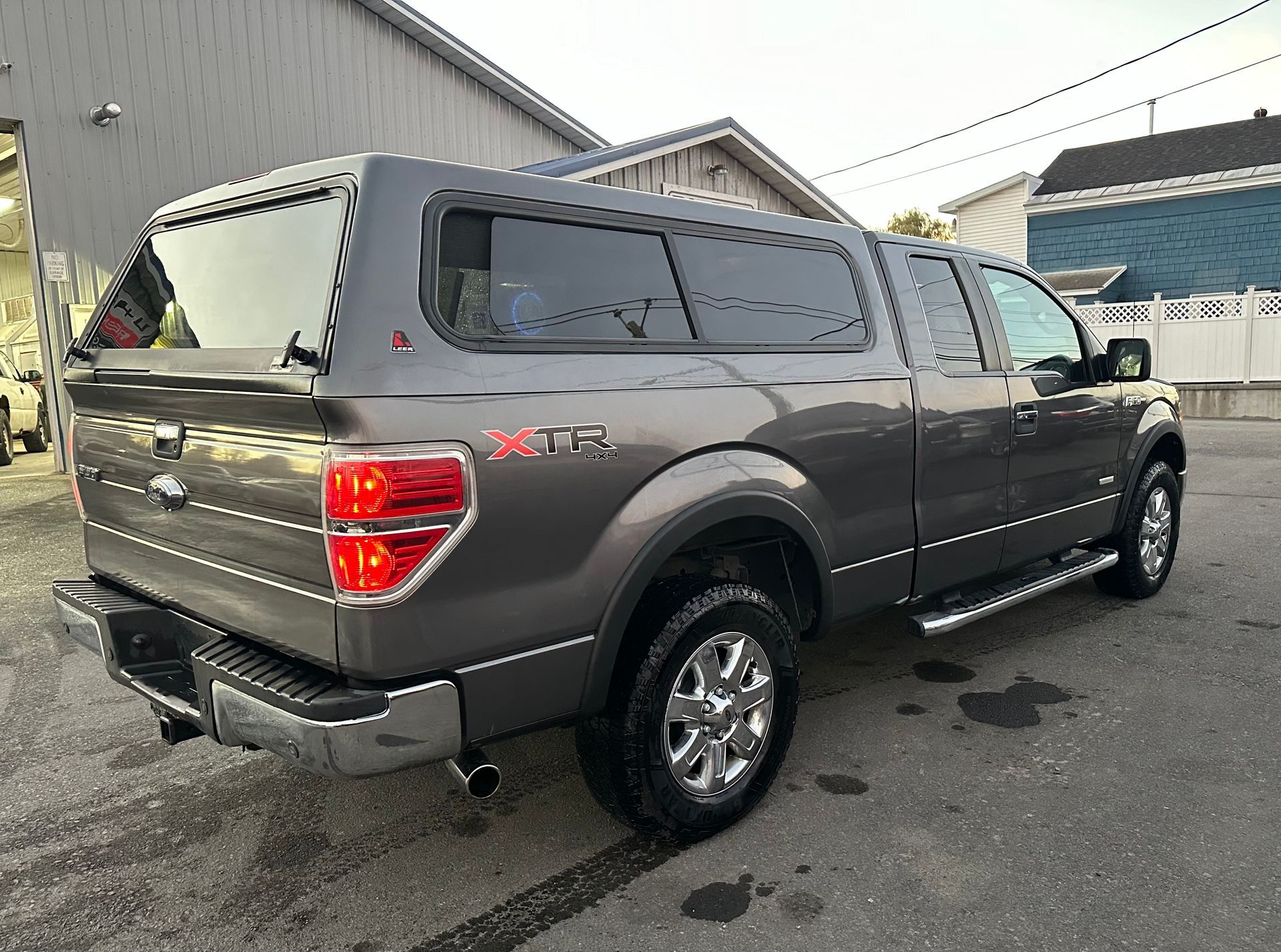 A gray truck with a canopy on top of it is parked in a parking lot.