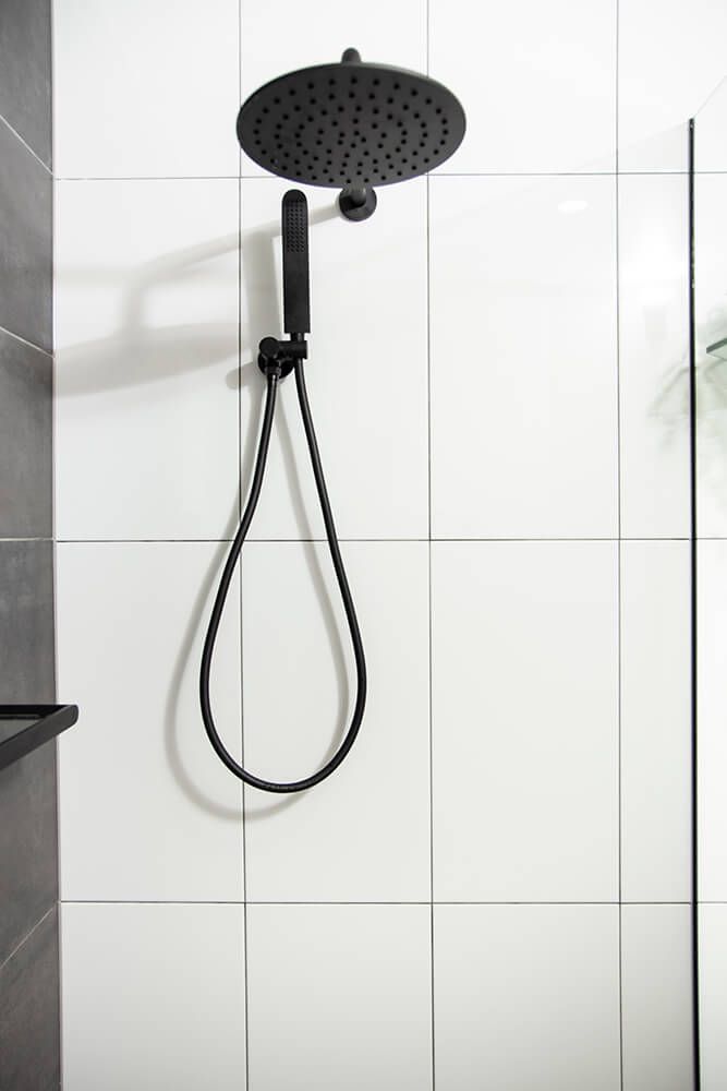 A Black Shower Head is Hanging From a White Tiled Wall in a Bathroom — Omni Builders In Bungalow, QLD