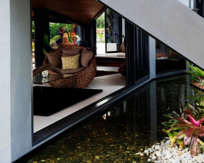 A Wicker Chair Sits in a Living Room Next to a Pond — Omni Builders In Bungalow, QLD