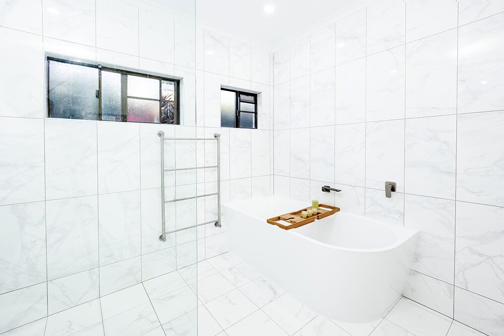 A Bathroom With White Tiles and a Bathtub — Omni Builders In Bungalow, QLD