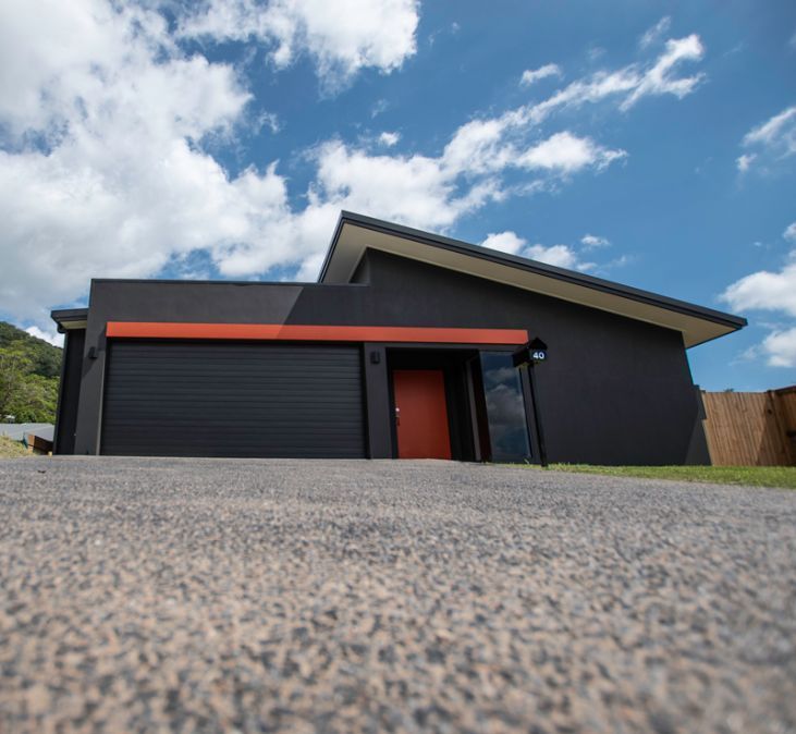 A Black House With a Red Door is Sitting on Top of a Concrete Driveway — Omni Builders In Bungalow, QLD