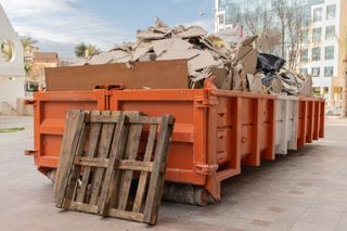 A large orange dumpster filled with cardboard and a wooden pallet.