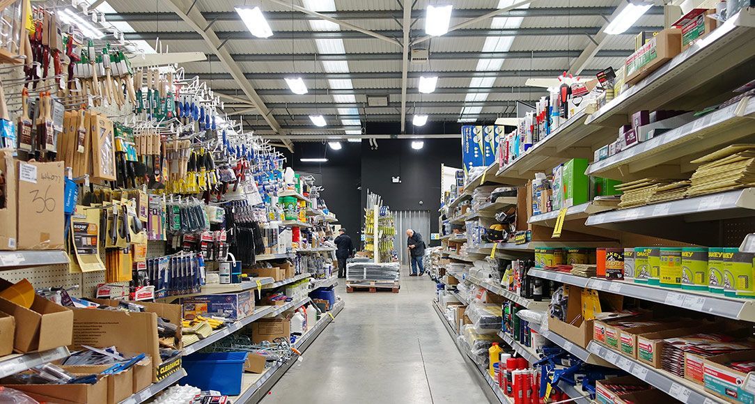 Hardware store interior, shelves stocked with tools and supplies, shoppers in the aisle.