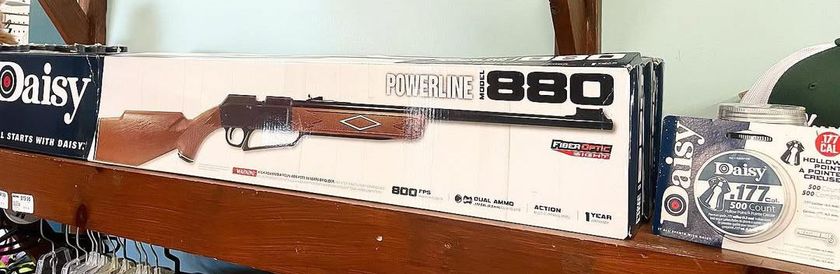 Box of a Daisy BB gun on a wooden shelf, with the model name 