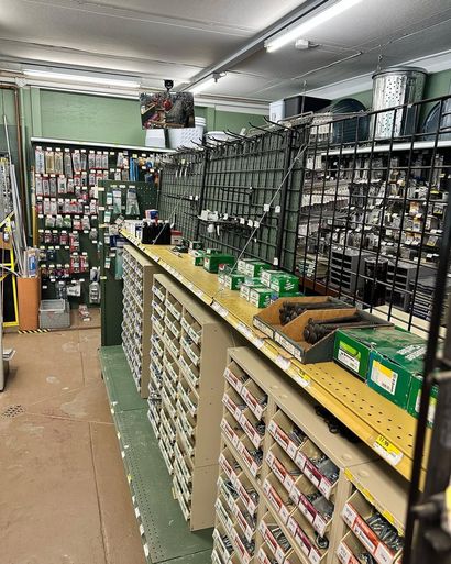 Interior of a hardware store. Aisles lined with shelves of hardware supplies, including boxes and various tools.