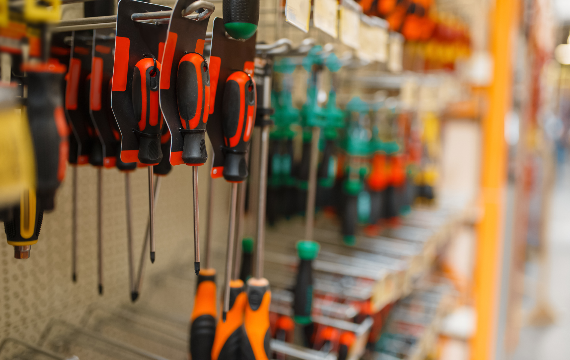 Screwdrivers hanging on display at a hardware store; orange and green handles, chrome shafts.