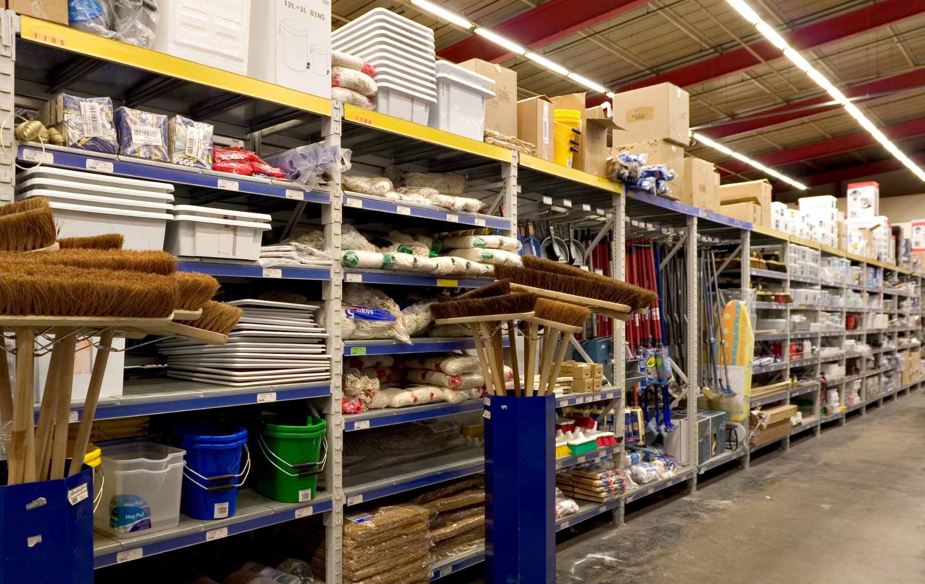 Hardware store interior with shelves stocked with items; brooms in foreground.