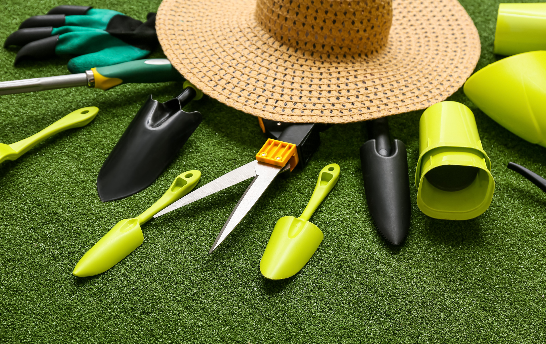 Gardening tools and straw hat on green grass.