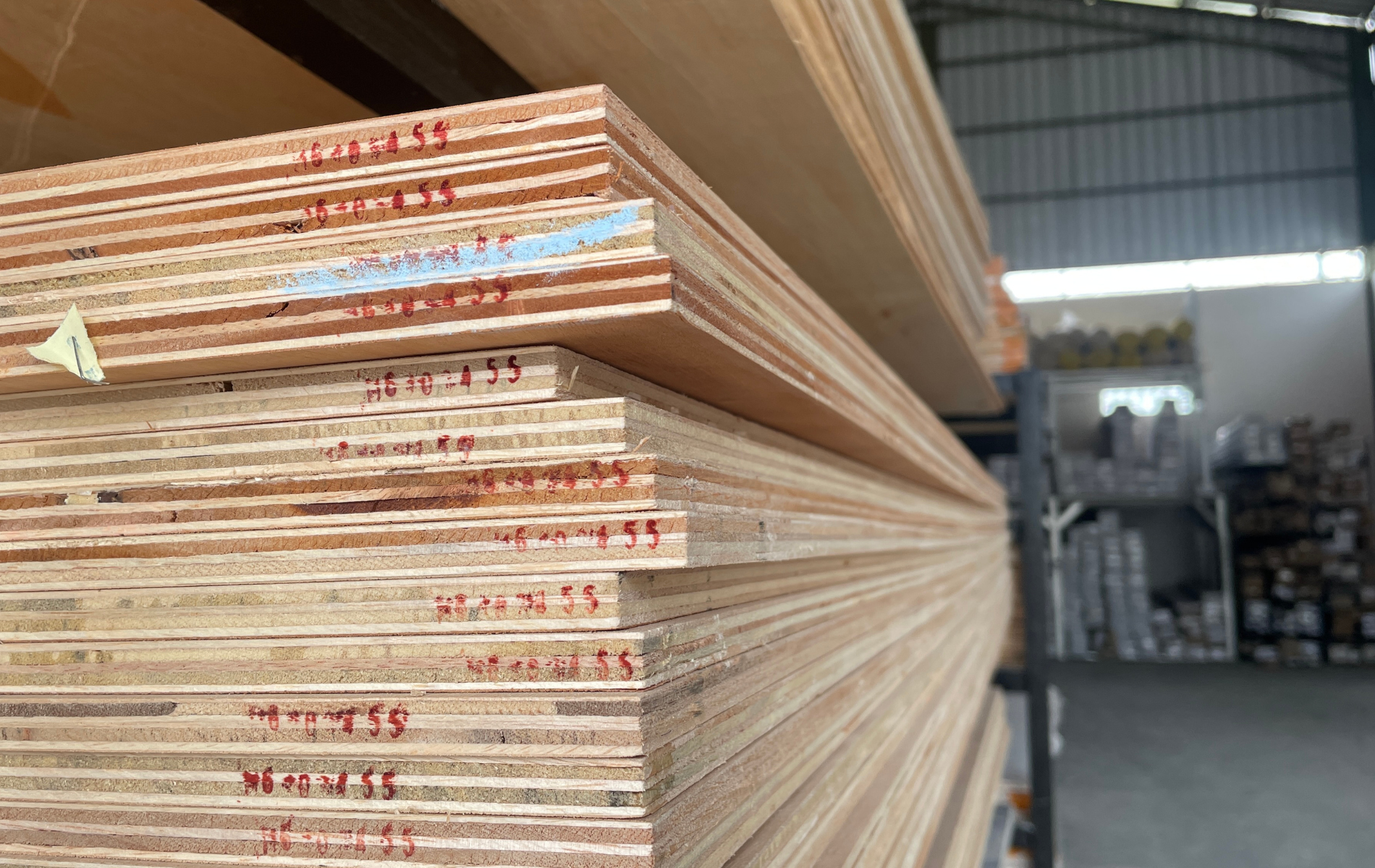 Stack of plywood sheets in a warehouse, showing layered wood grain and markings.