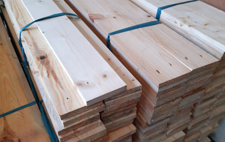 Stacks of light-colored wooden planks bound with blue straps, ready for construction.
