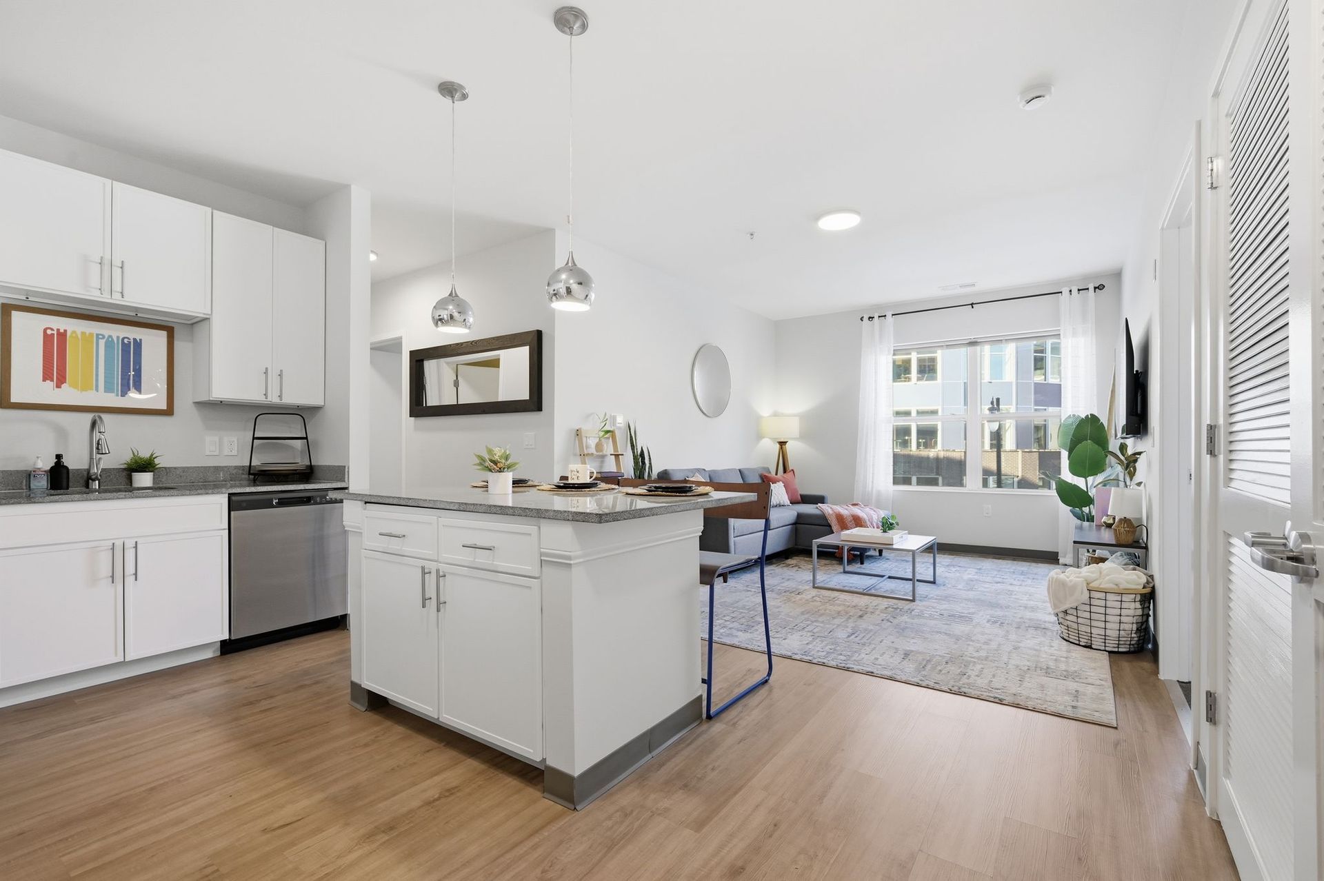 Bright, modern apartment interior. Kitchen island, white cabinets, stainless appliances, living area with couch, rug, window.