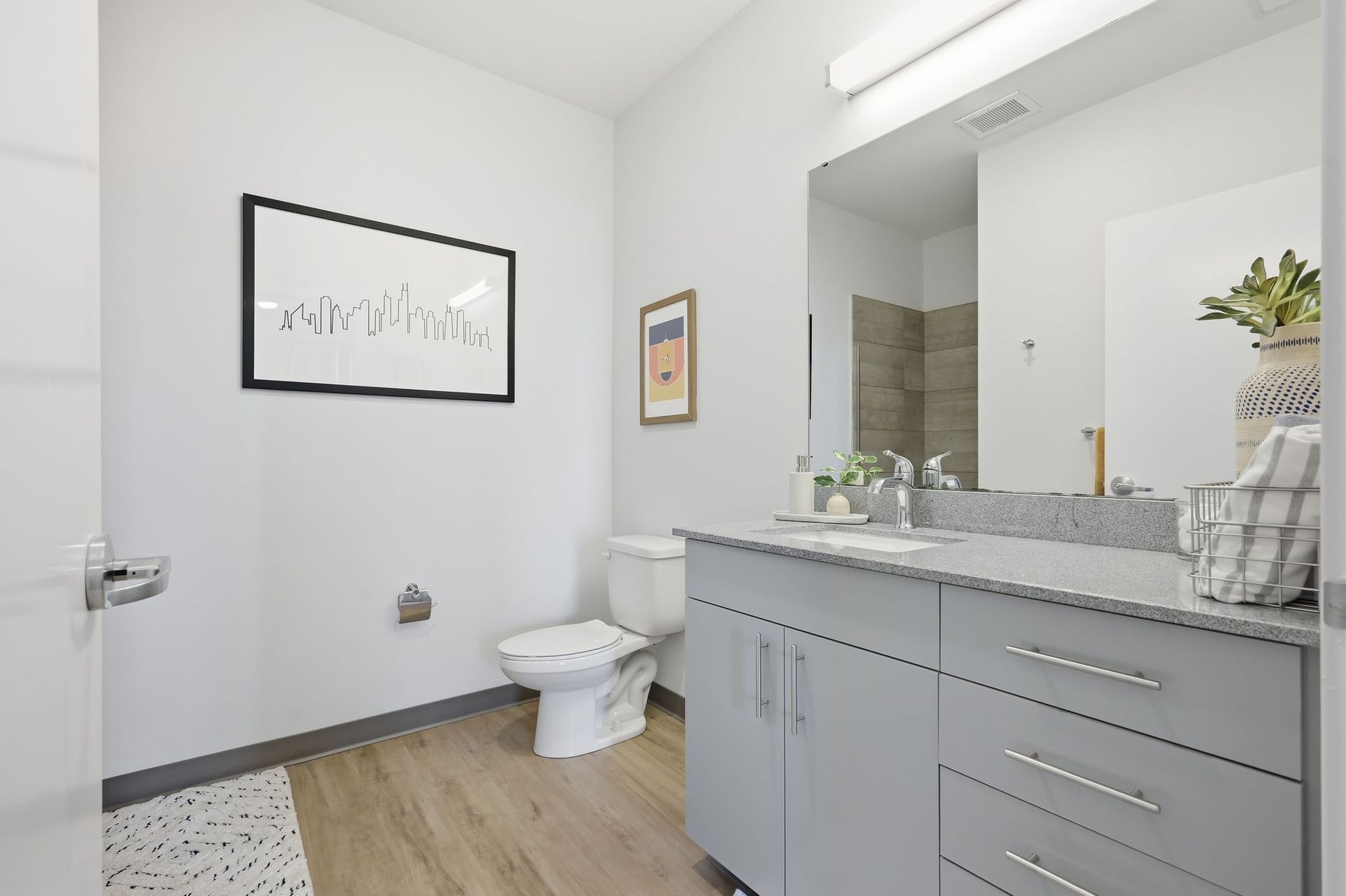 Bathroom with gray vanity, toilet, mirror, artwork, and white walls.