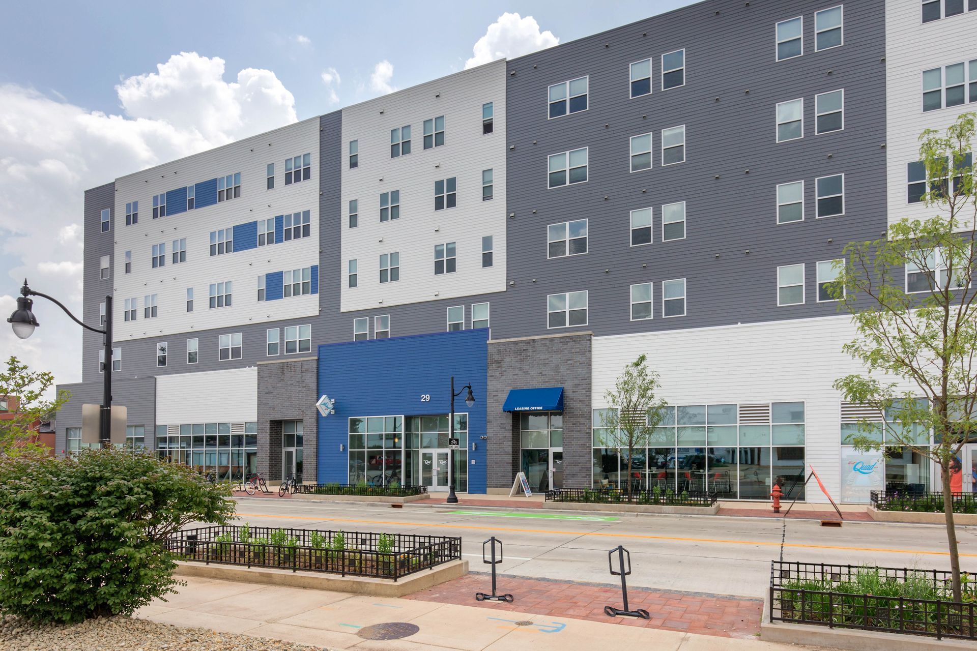 Modern multi-story building with commercial storefronts; blue, gray, and white facade.