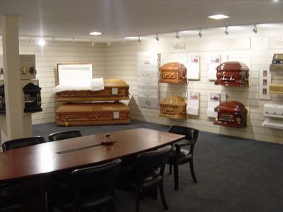 Funeral home showroom with caskets on display and a table with chairs for consultation.