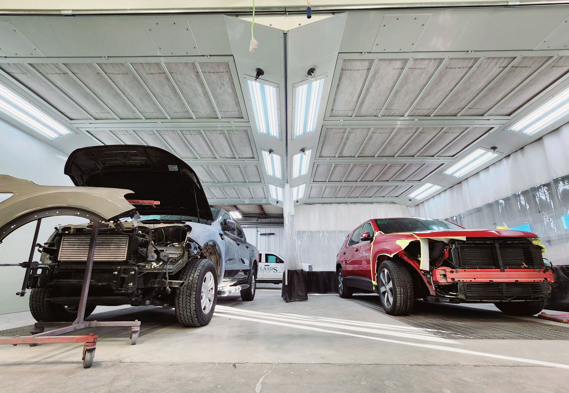 Cars in various stages of repair inside a brightly lit auto body shop.