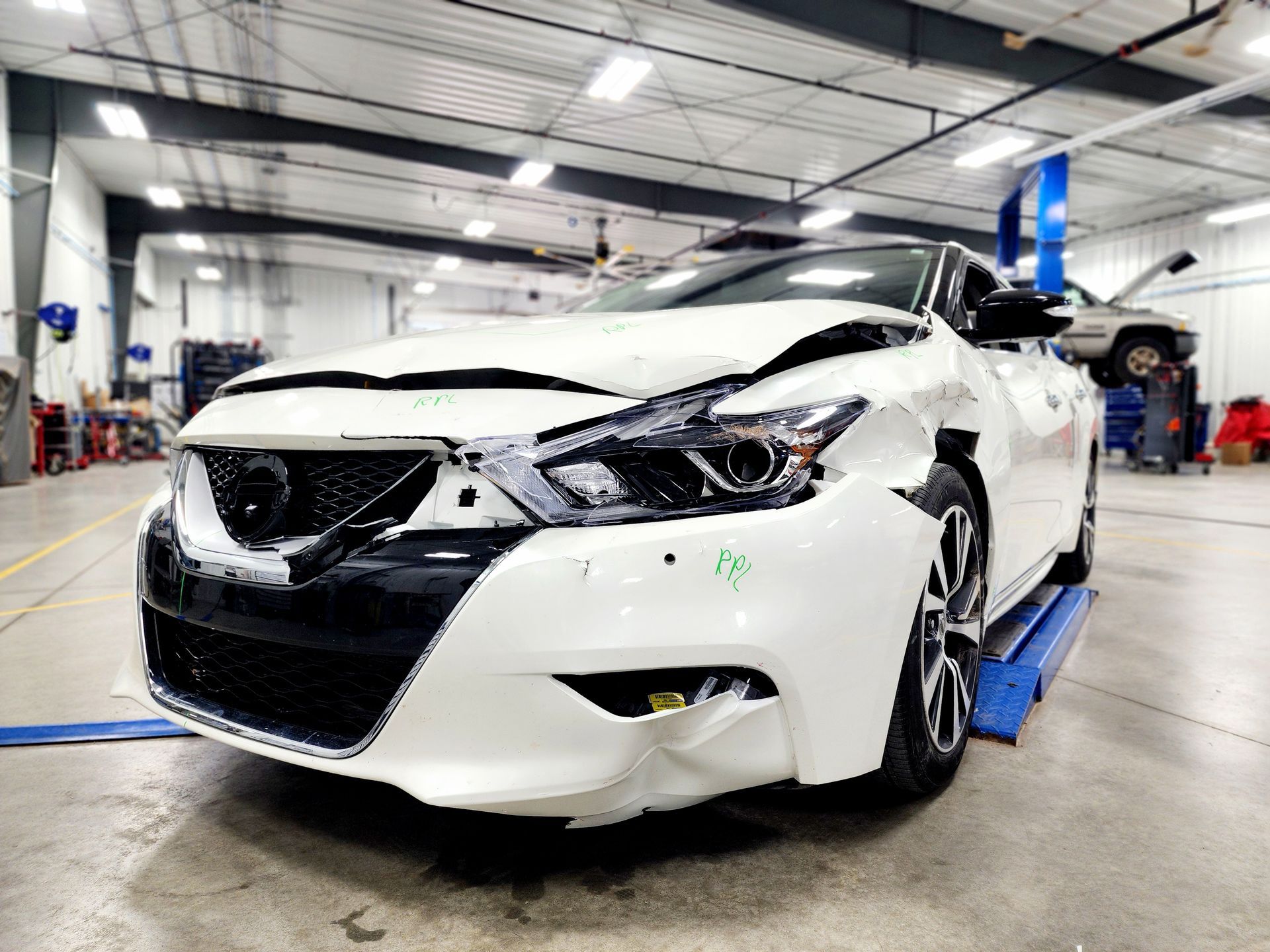 A white nissan maxima is sitting on a lift in a garage.