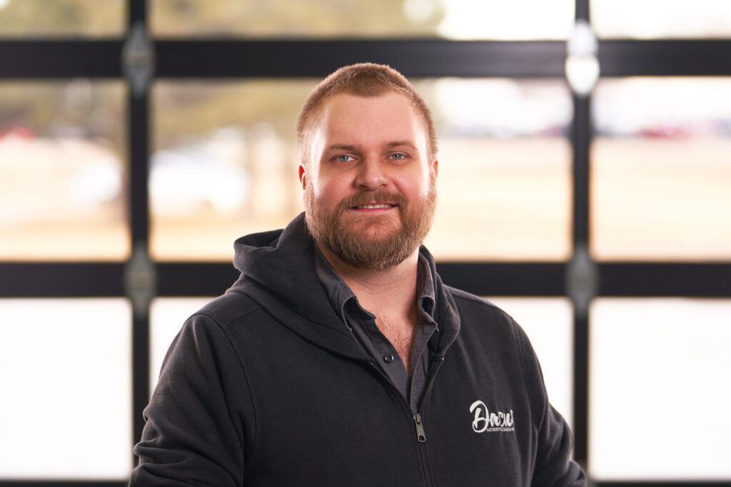 A man with a beard is standing in front of a garage door.