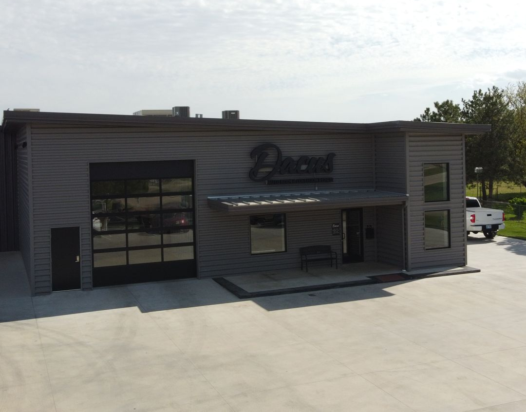 Modern gray building with glass garage door and entrance under a small awning; 