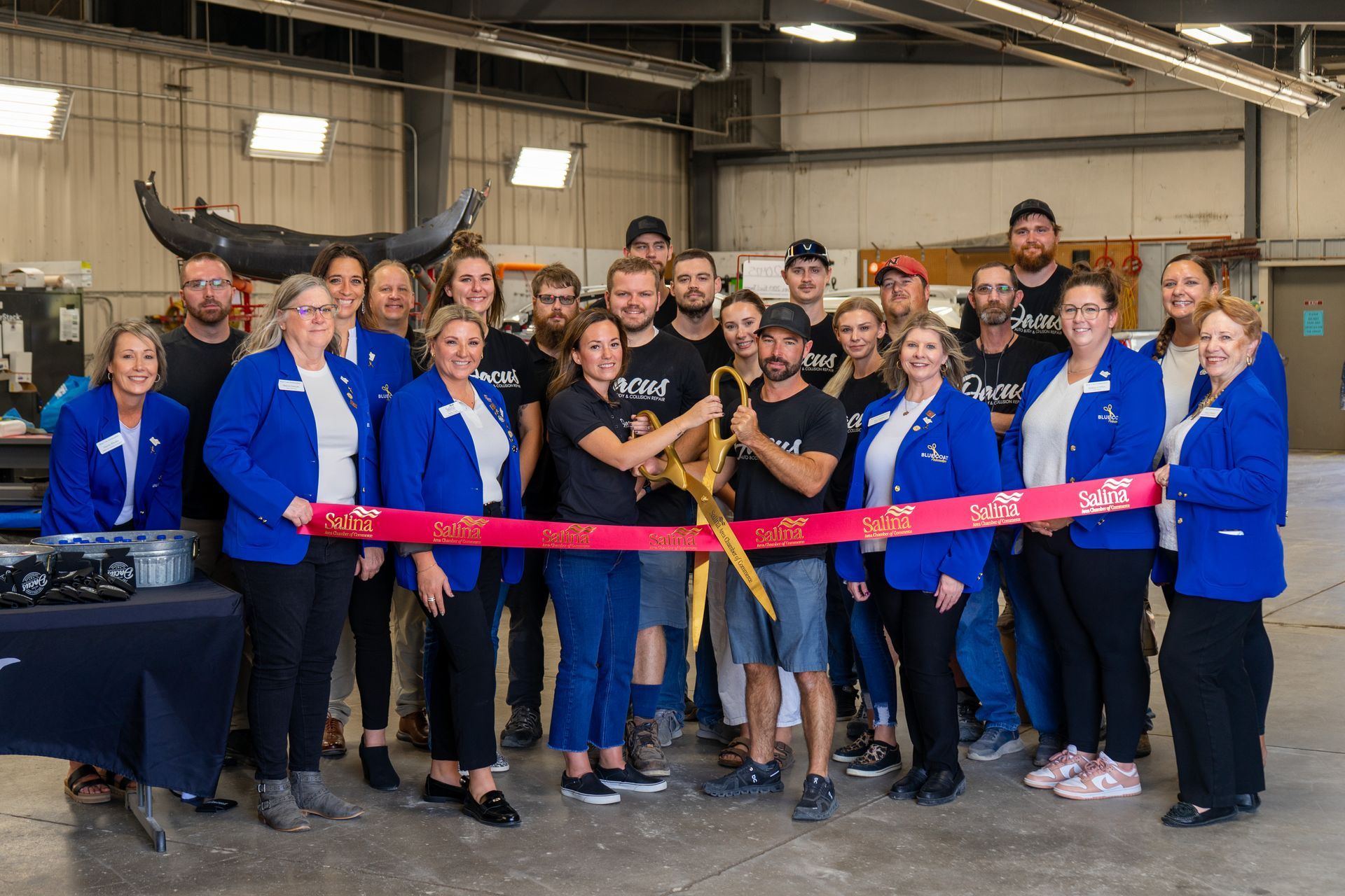 People cutting a ribbon at an event in a workshop. A gold scissor cuts a red ribbon, others watch, some smile.