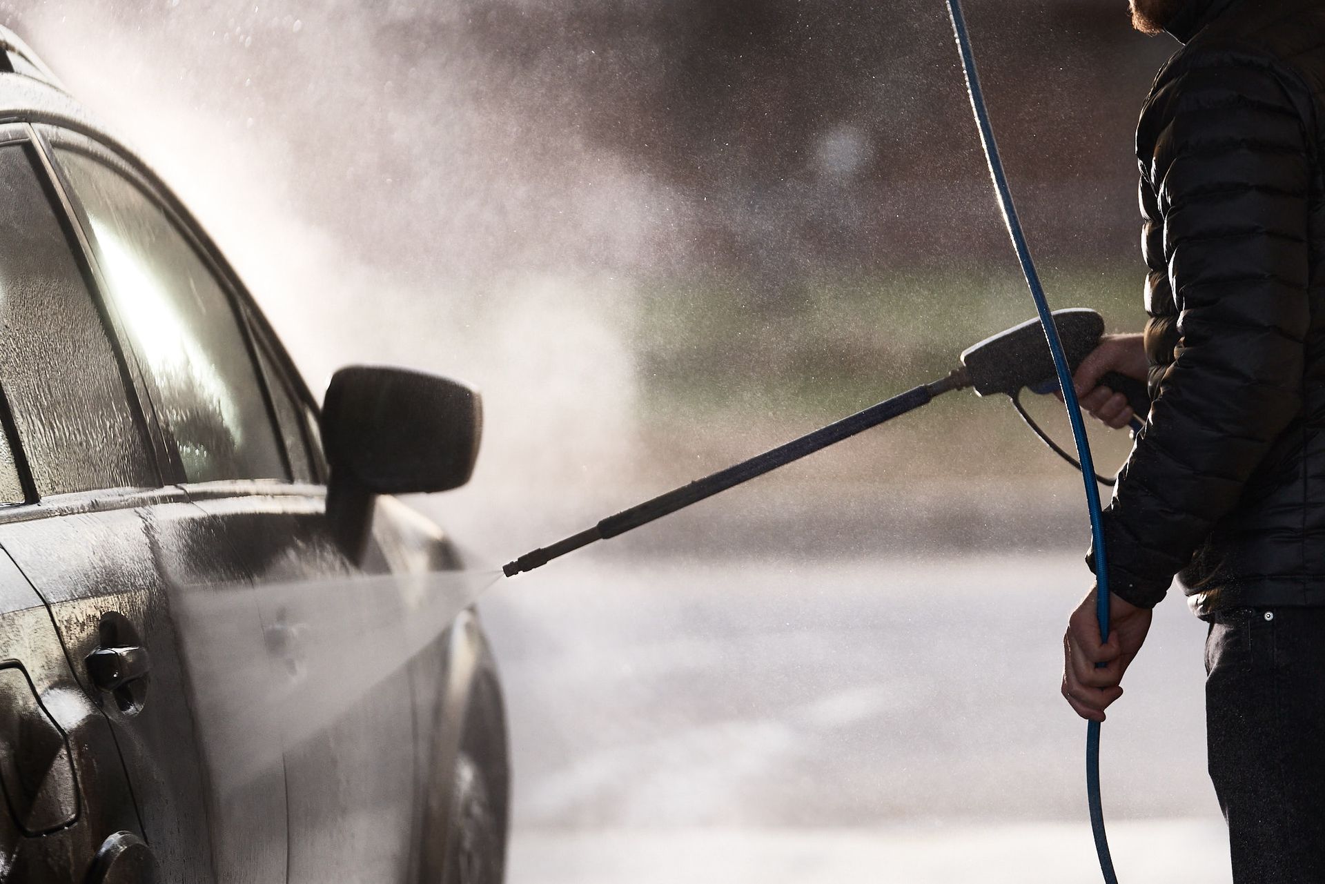 A man is washing a car with a high pressure washer.