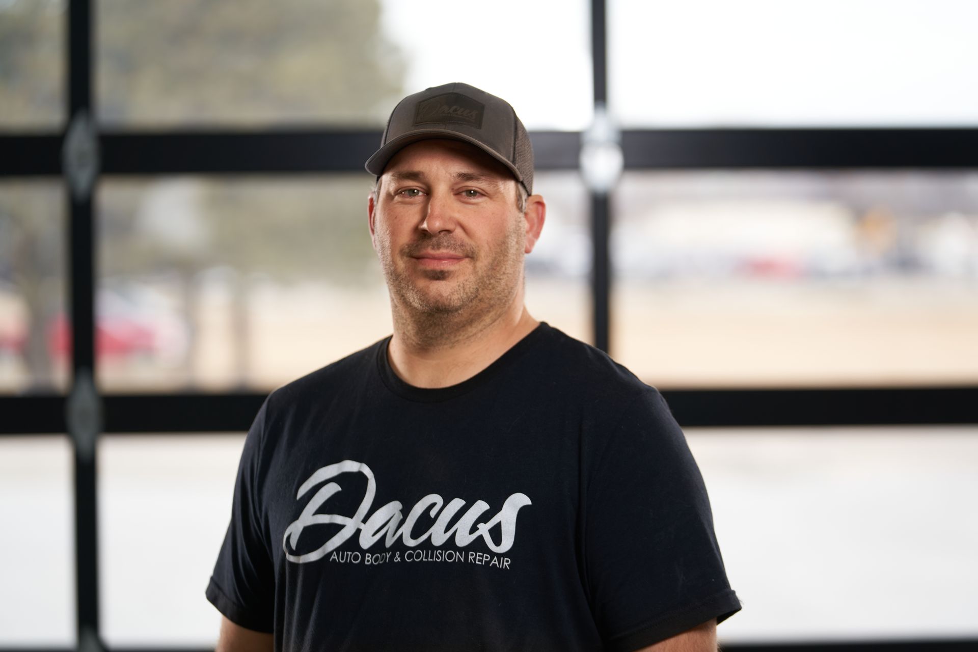 A man wearing a black t-shirt and a hat is standing in front of a garage door.