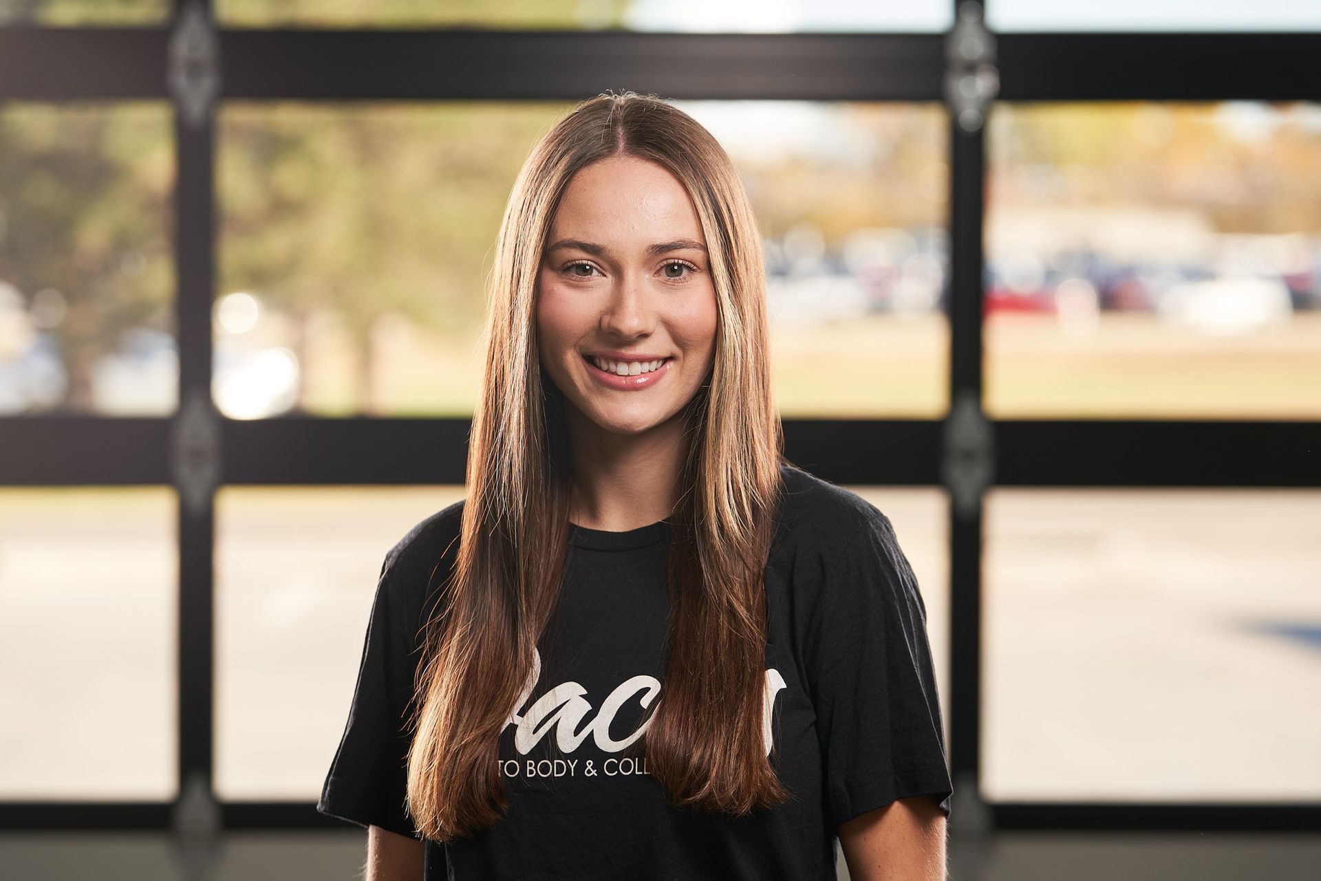 A young woman wearing a black t-shirt is smiling in front of a garage door.