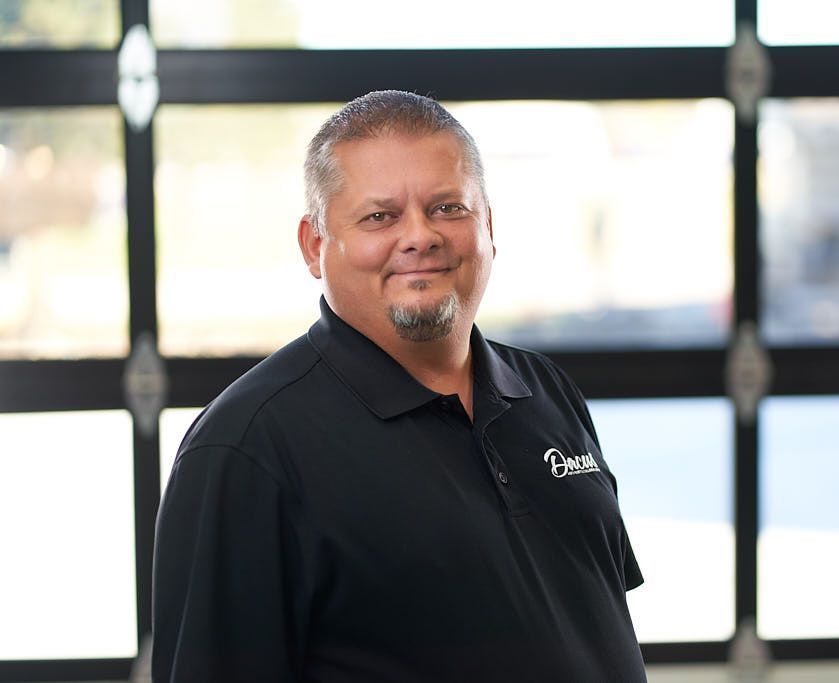 A man in a black shirt is standing in front of a garage door.