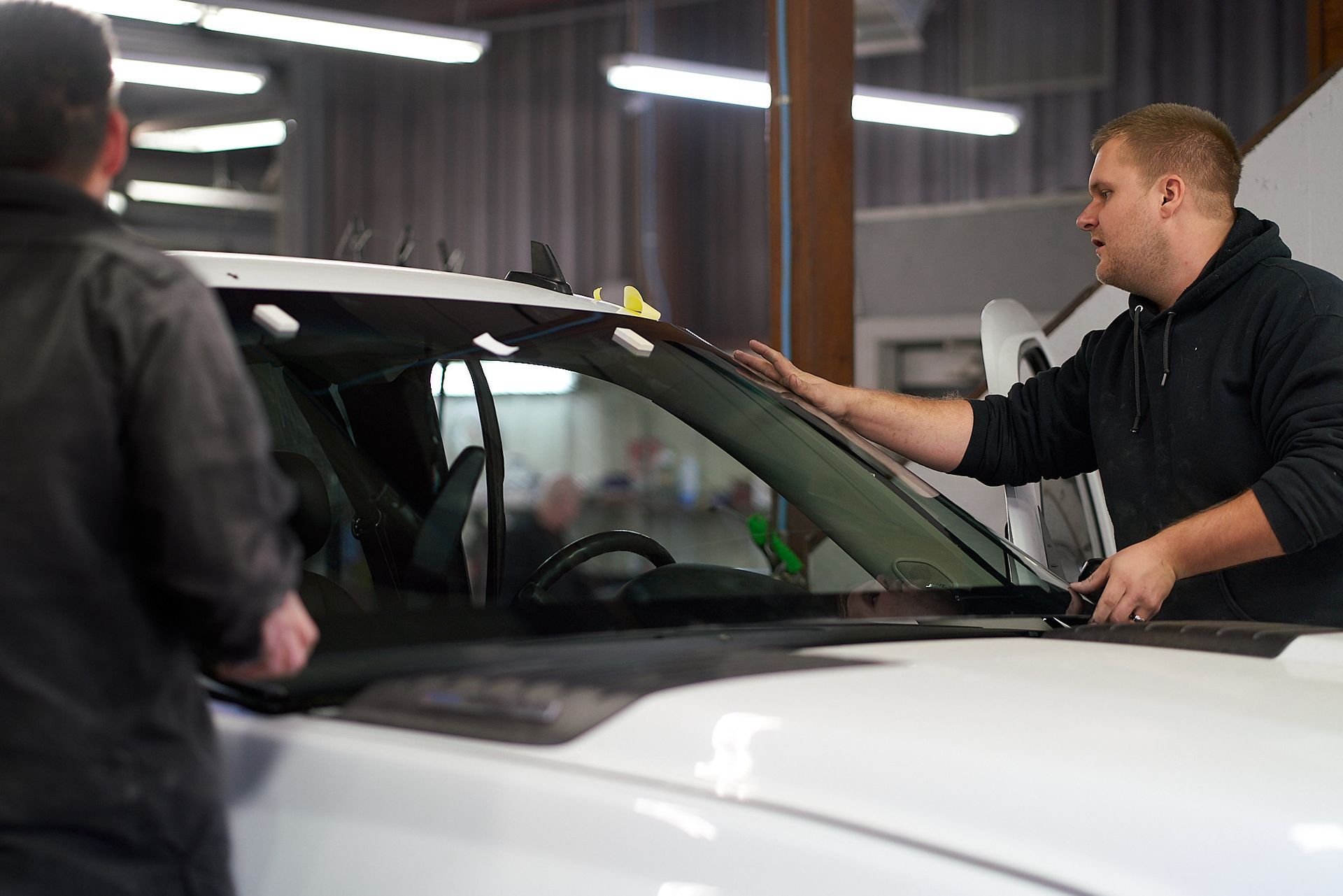 Two men installing a windshield on a white truck inside a garage.
