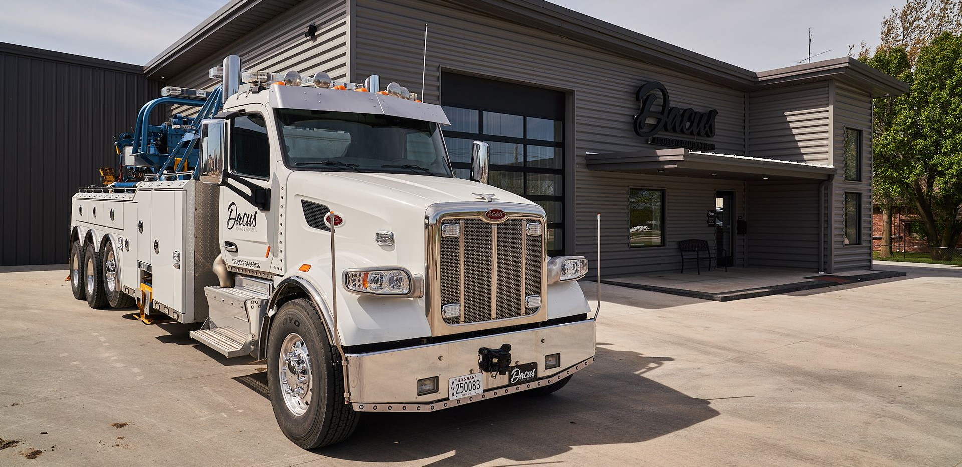 White tow truck parked in front of a gray building with the name 
