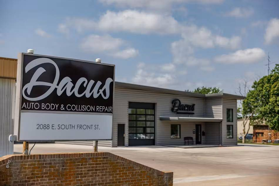 Dacus Auto Body & Collision Repair building with sign. Gray and black exterior, cloudy sky.