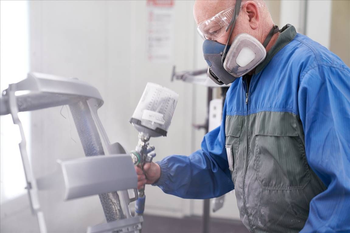 Man in protective gear spray-painting a chair, indoors.