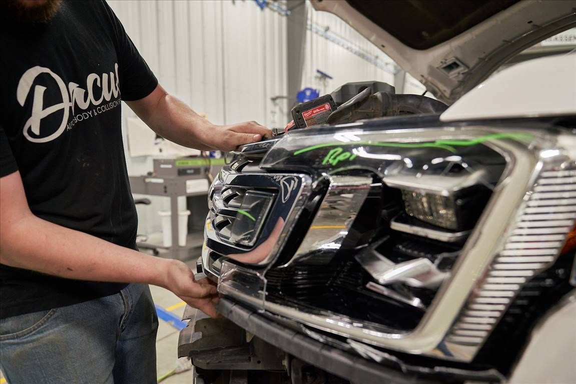 Man installing chrome bumper on a white truck, in a workshop.