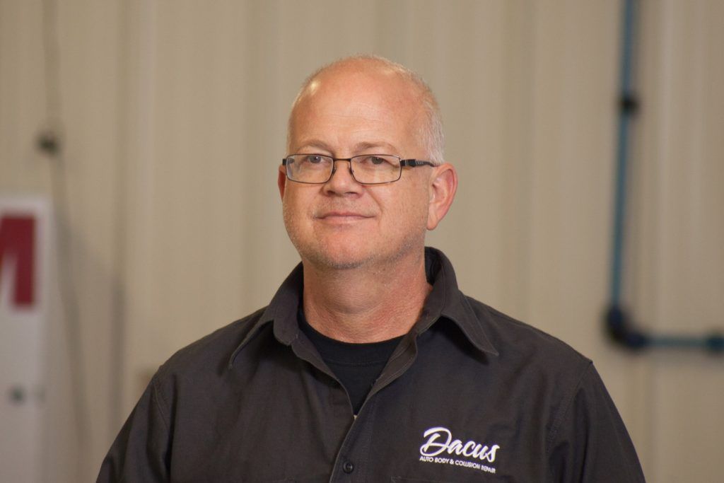 A bald man wearing glasses and a black shirt is standing in front of a white board.