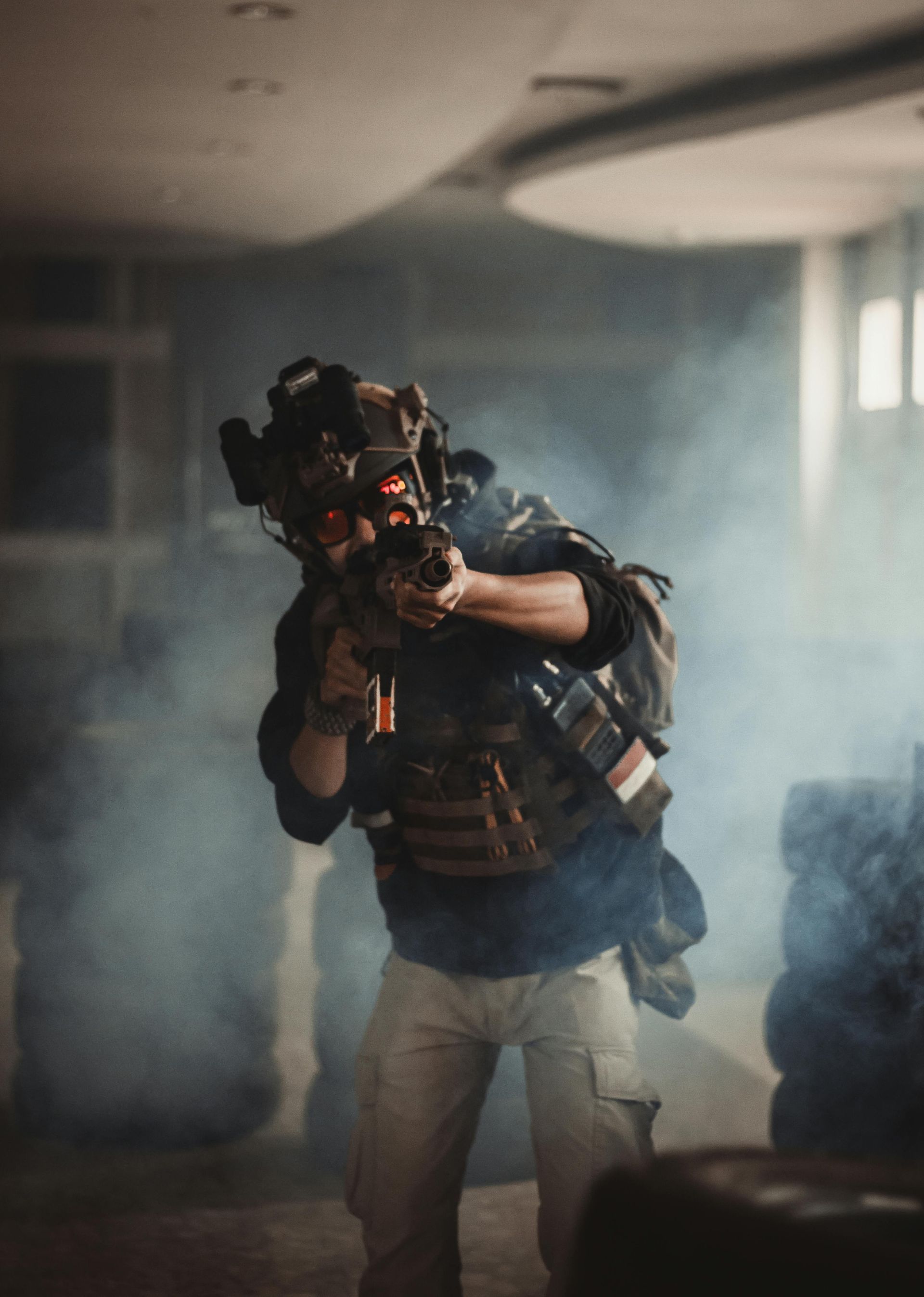Soldier aiming rifle with red laser sight in a dark, smoky indoor setting.