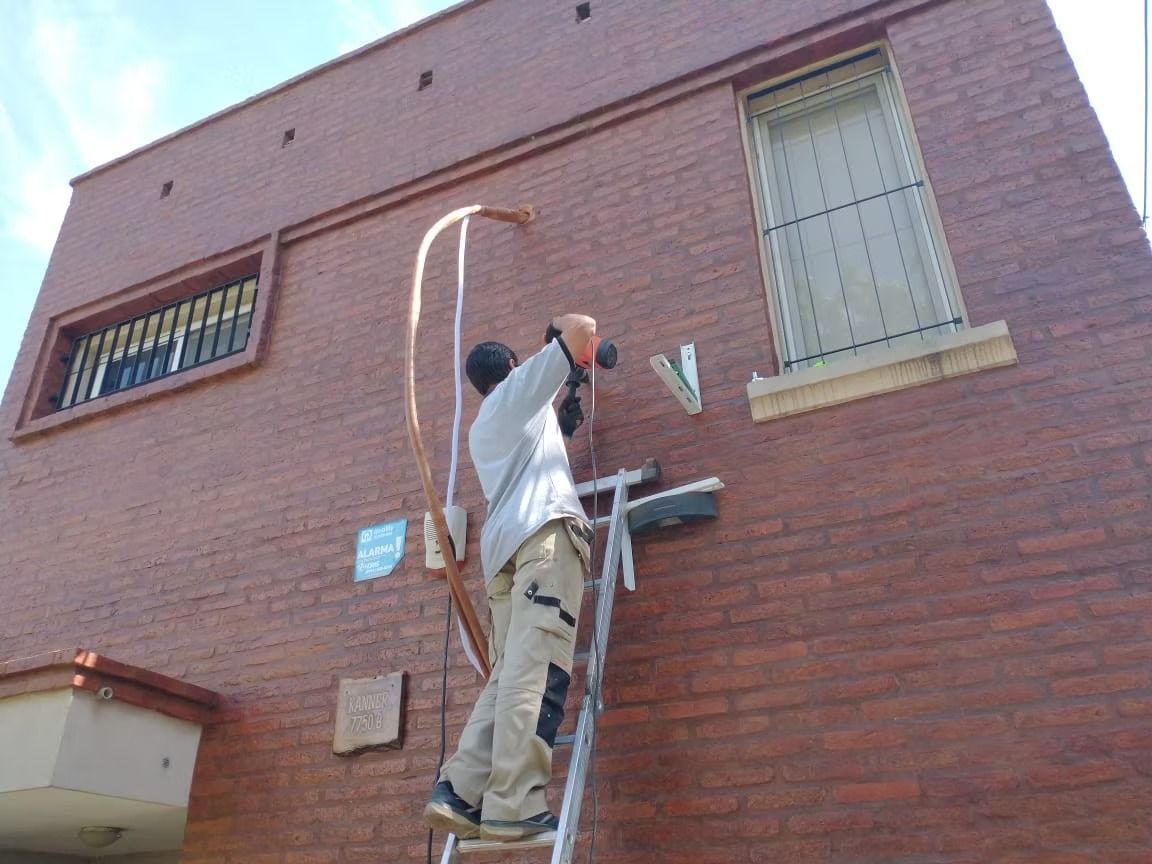 Una persona en una escalera instalando tuberías de cobre en el exterior de un edificio de ladrillo.