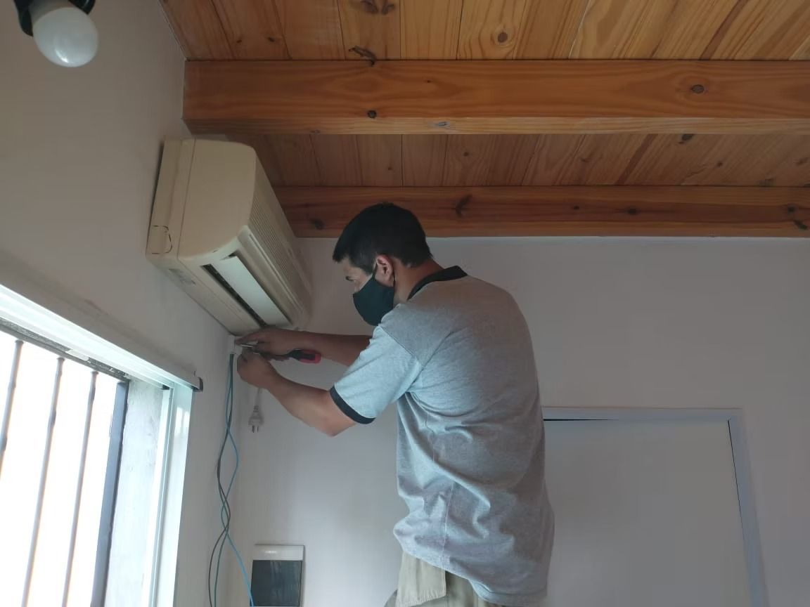 Hombre con mascarilla instalando un aparato de aire acondicionado en un interior. 