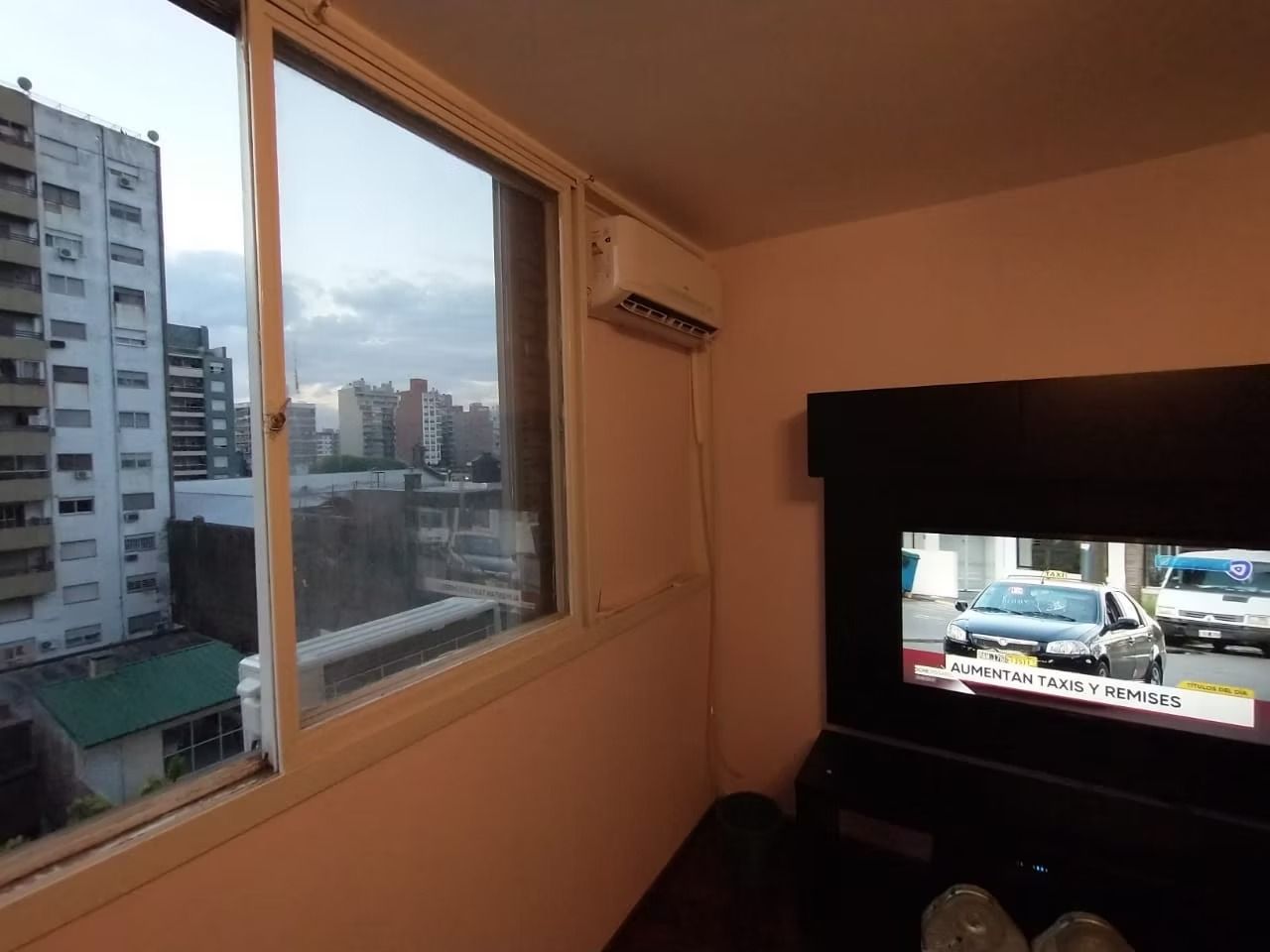 Habitación con ventana, televisor y edificios al aire libre