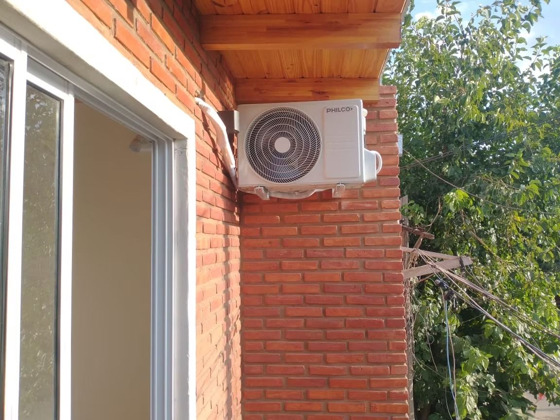 Unidad de aire acondicionado montada en el exterior de un edificio de ladrillo rojo junto a una ventana.