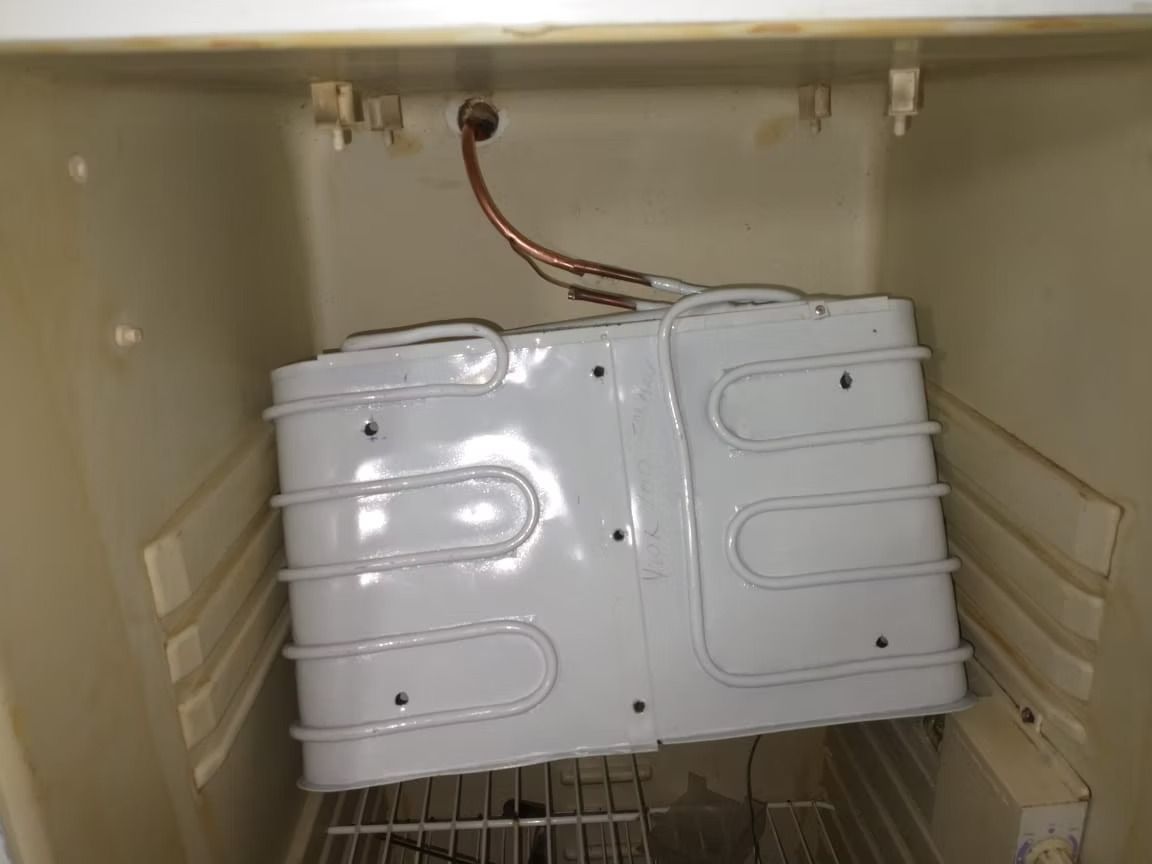 Serpentín de refrigerador blanco en una cavidad de refrigerador vacía de color beige con tubos de cobre.