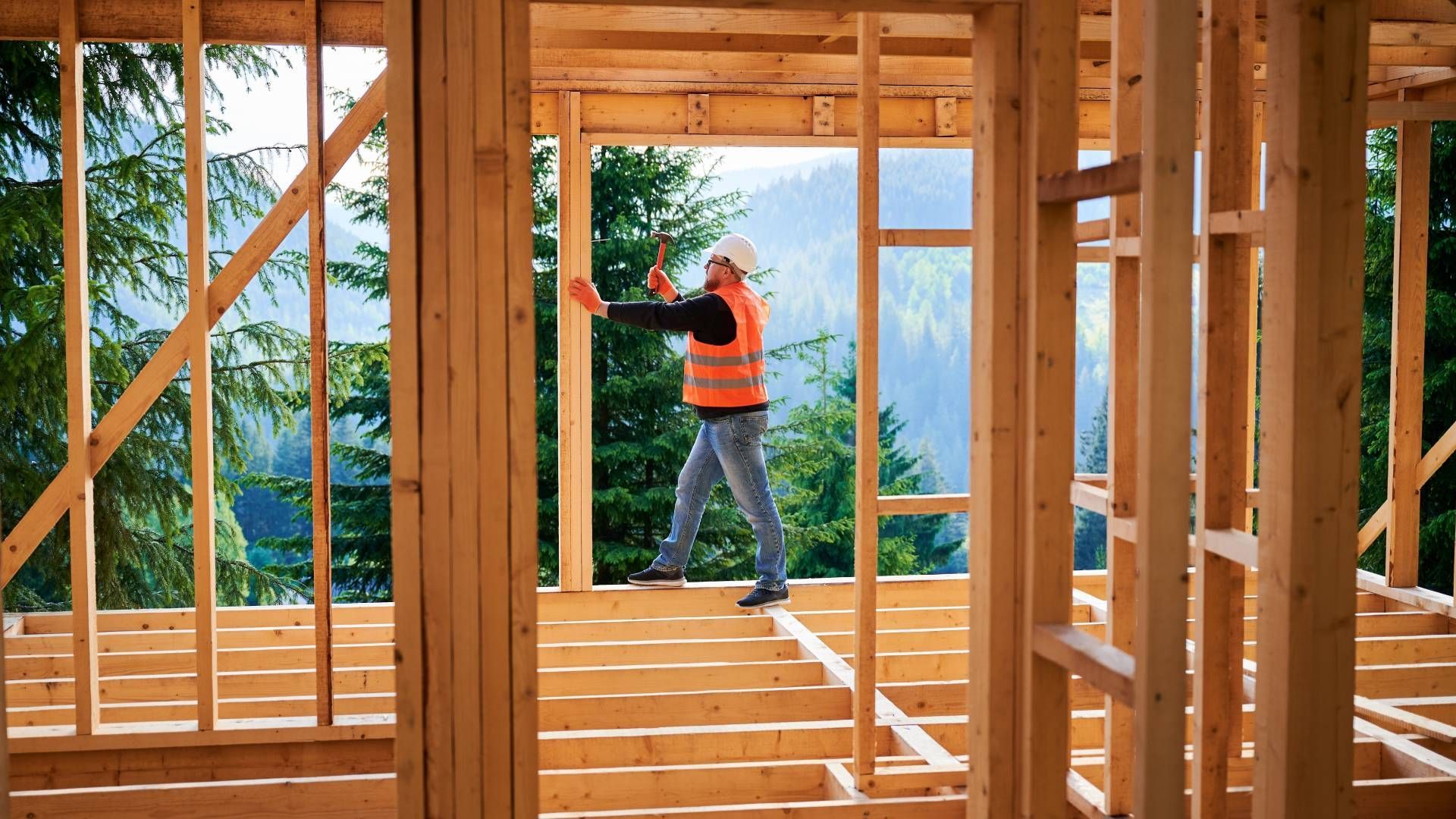A man is standing in a wooden frame of a house under construction.